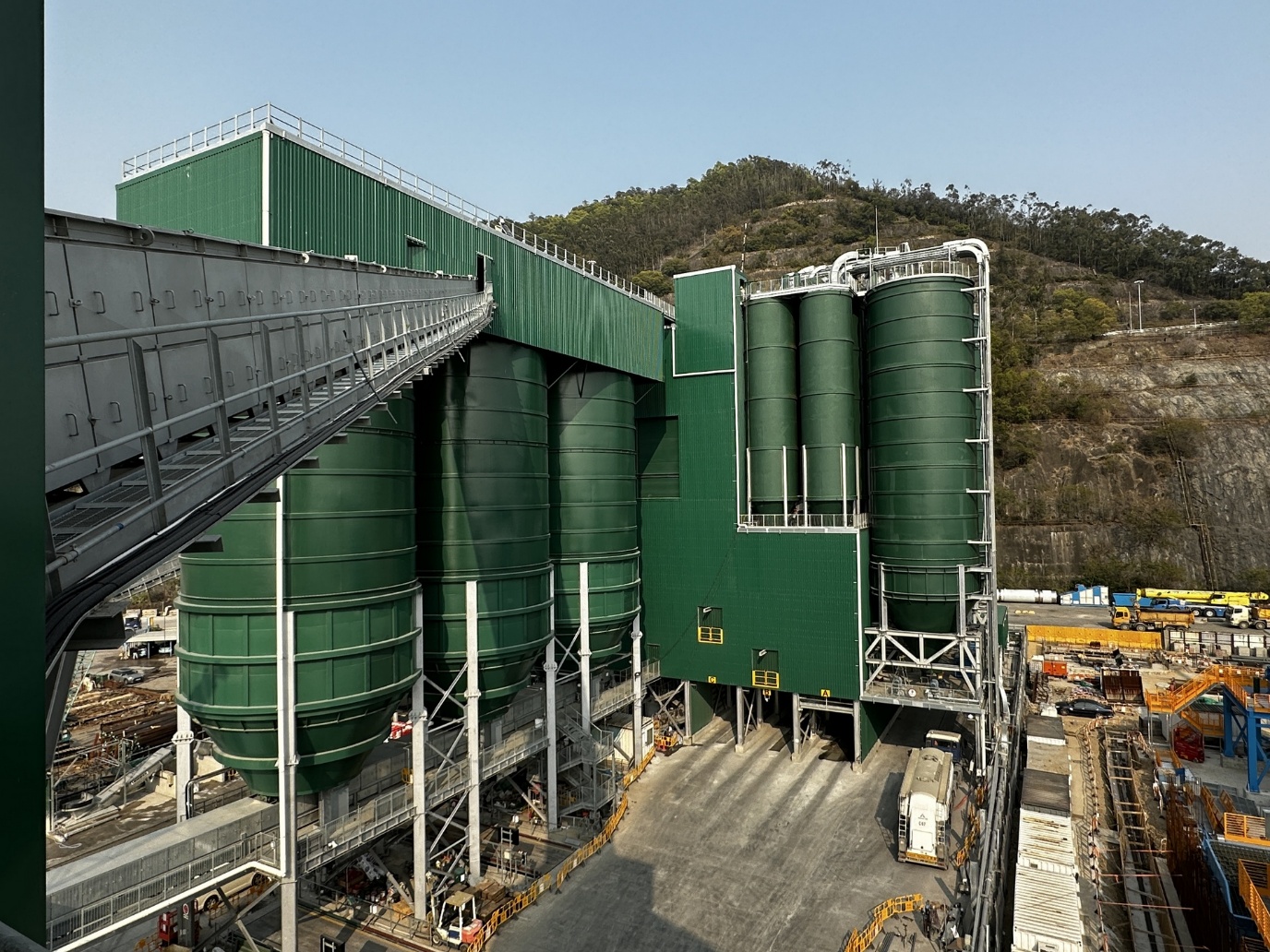 Large green concrete batching plant with silos and enclosed process structures in Hong Kong